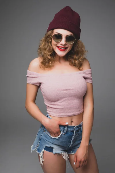 Стильный модный портрет трезвенной случайной молодой женщины в солнцезащитных очках и шляпе хипстера в студии — стоковое фото