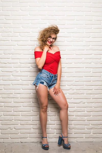 Gülümseyen ifade genç yetişkin kadın tuğla duvara yaslanmış tam uzunlukta portresi