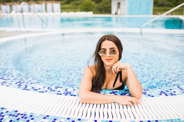 Mulher sexy bonita relaxando na água da piscina desfrutando do sol de verão no dia quente de verão na borda da piscina — Fotografia de Stock