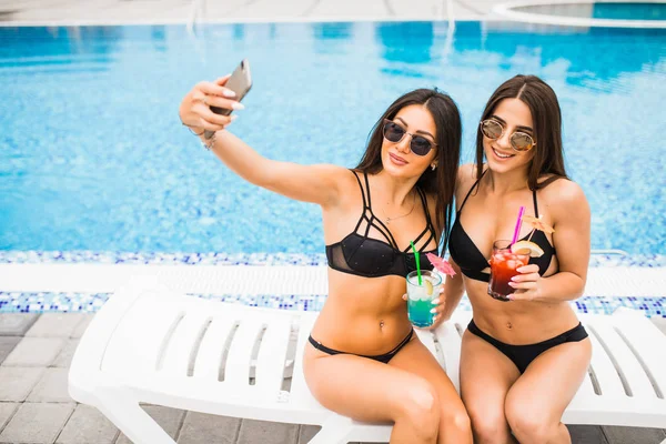 İki çekici esmer kadın poz bikini giyen selfie fotoğraf yapma Yüzme Havuzu yakınlarında. Yaz saati