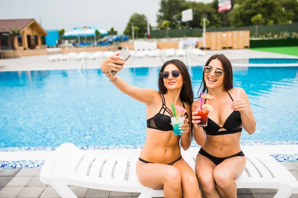 İki çekici esmer kadın poz bikini giyen selfie fotoğraf yapma Yüzme Havuzu yakınlarında. Yaz saati