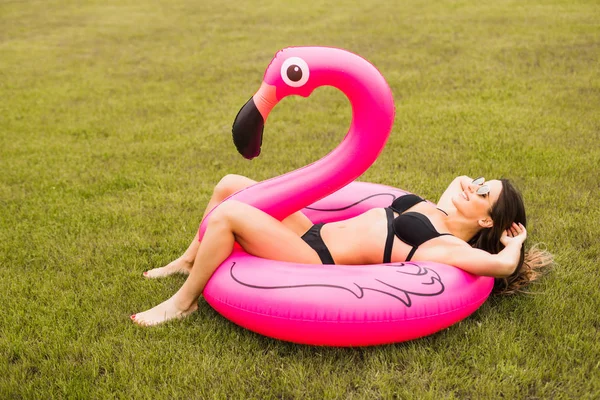 Jong en sexy meisje met plezier en lachen en plezier op het gras in de buurt van het zwembad op een opblaasbaar roze flamingo in een badpak in de zomer — Stockfoto