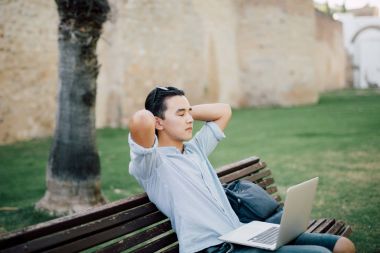 Parkta üzerinde oturan genç Asyalı adam laptop ile tezgah ve iyi bir ruh hali ile bitmiş işten sonra rahatla