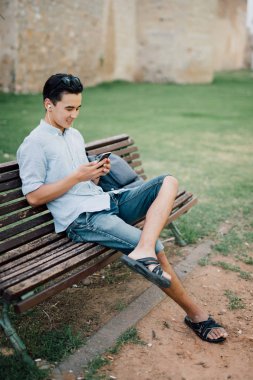 Bir parkta bir bankta oturmuş bir akıllı telefon kullanarak mutlu Asya'ya ait adam 