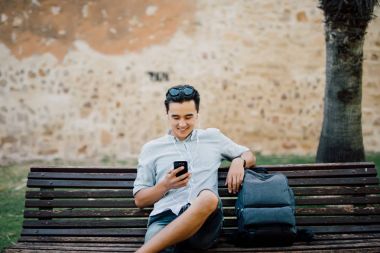 Bir parkta bir bankta oturmuş bir akıllı telefon kullanarak mutlu Asya'ya ait adam 