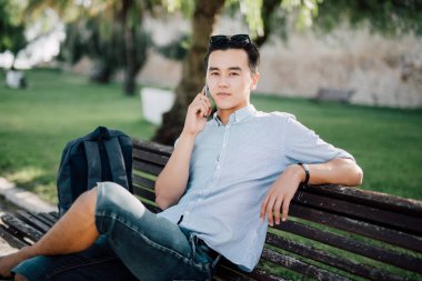 Telefonda konuşurken parktaki bankta otururken yakışıklı Asya öğrenci adam