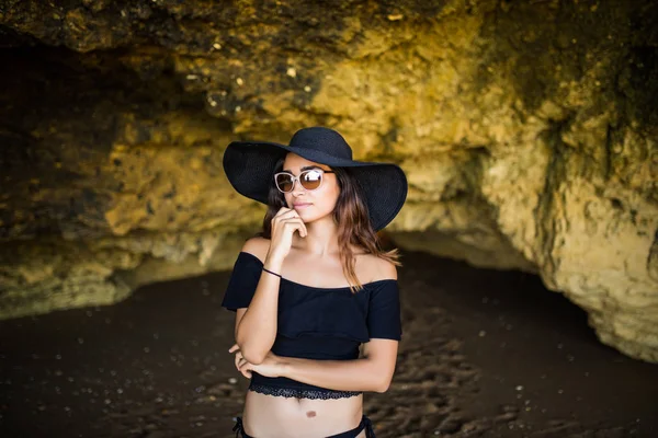 想用帽子和太阳镜夏天职业准时在岩石海滩上晒日光浴的拉丁美女 — 图库照片