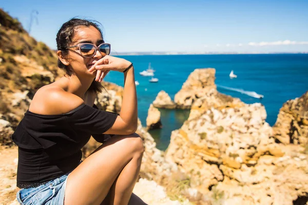 Menina Latina sentada em um penhasco e desfrutar da hora de verão perto do oceano Atlântico em Portugal — Fotografia de Stock