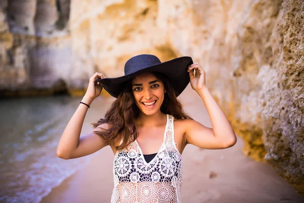 Portrait de belle fille latine sur la plage avec chapeau noir sourire océan soigné et rochers sur vocation estivale — Photo
