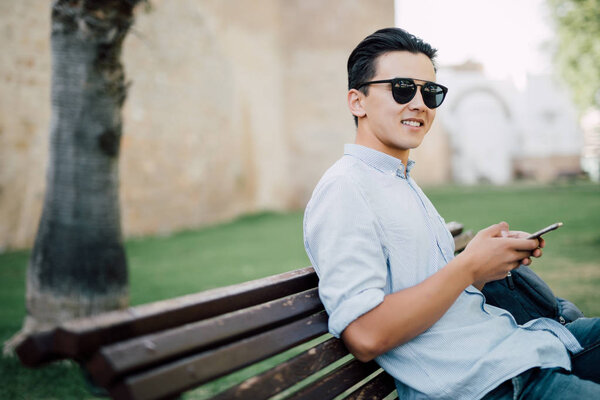 Handsome asian Man using cellphone on a bench in the park 