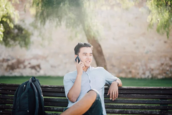 Telefonda konuşurken parktaki bankta otururken yakışıklı Asya öğrenci adam