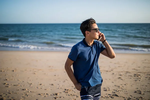 Молодой азиат разговаривает по телефону и видит закат в тропиках — стоковое фото