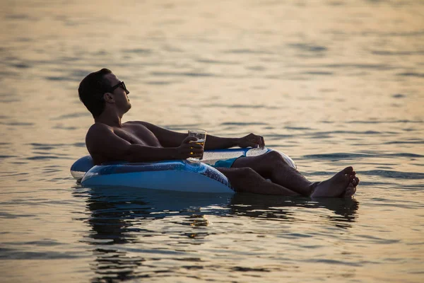 Мужчина расслабляется в океанской воде на резиновом кольце пьет пиво и наслаждается призванием. Летнее призвание — стоковое фото