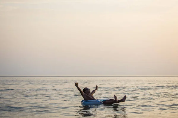 Hombre con las manos levantadas sonríe y disfruta del verano en anillo de goma en el agua de mar. Vocación de verano . — Foto de Stock