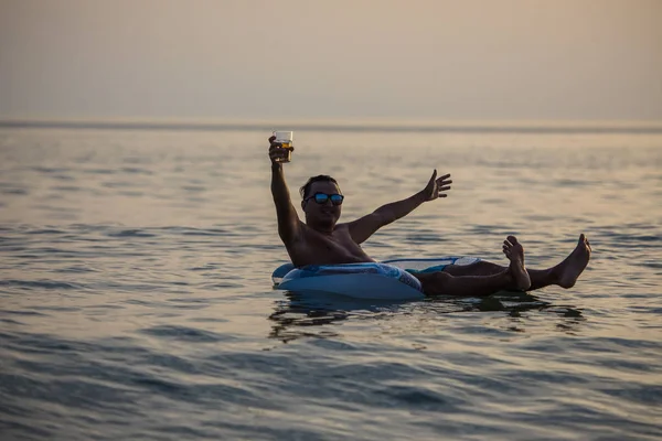 Hombre con las manos levantadas sonríe y disfruta del verano en anillo de goma en el agua de mar. Vocación de verano . — Foto de Stock