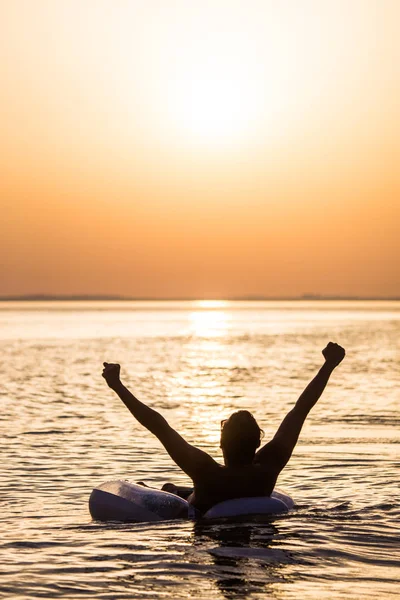 Joven feliz con las manos levantadas flotando en el anillo inflable en el agua del océano en la puesta del sol. Hombre disfrutar de la vocación de verano con las manos en el agua del océano . — Foto de Stock