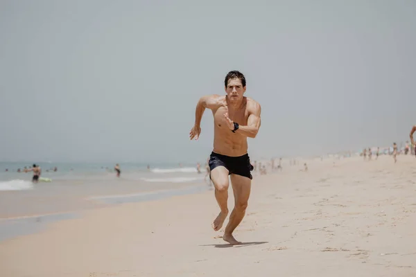 Jonge man met het lichaam van de atleet loopt langs het strand — Stockfoto