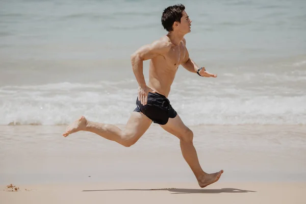 Пляжный спортсмен бегун проводит тренировку кардио. Здоровый образ жизни спортсмен мужского пола, занимающийся спортом на пляже на закате солнца с топлесс в шортах. — стоковое фото