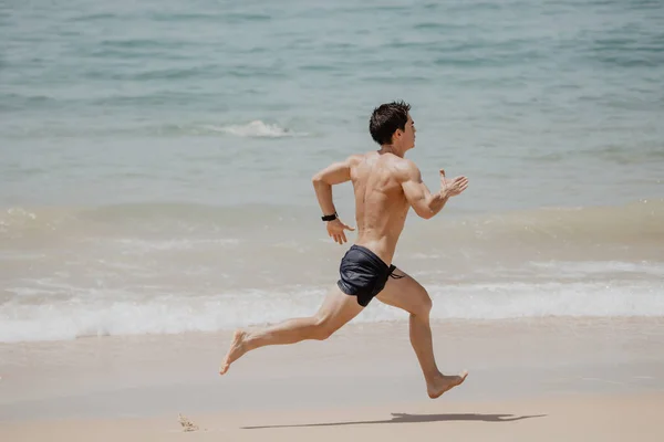 Пляжный спортсмен бегун проводит тренировку кардио. Здоровый образ жизни спортсмен мужского пола, занимающийся спортом на пляже на закате солнца с топлесс в шортах. — стоковое фото
