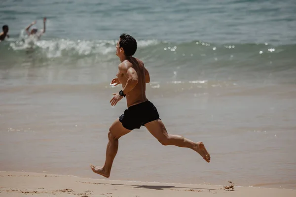 Jonge man met het lichaam van de atleet loopt langs het strand — Stockfoto