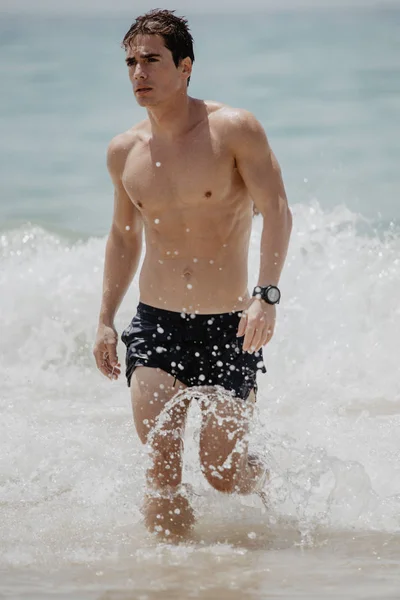 Jeune homme musclé qui sort de l'eau dans une plage tropicale en maillot de bain — Photo