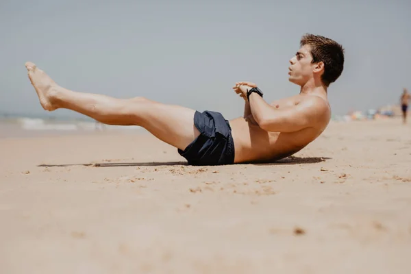 Retrato de vista lateral de un joven haciendo ejercicio en la playa haciendo abdominales — Foto de Stock