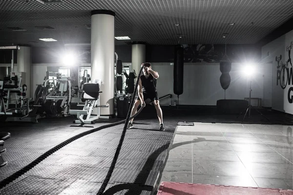 Fitness man working out with battle ropes at gym. Battle ropes fitness man at gym workout exercise fitted body. Fitness man training with battle rope in fitness club. Training with battle rope