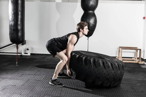 Entrenador personal volteando un neumático en un gimnasio mientras instruye a una modelo de fitness femenina cómo hacer el ejercicio . — Foto de Stock