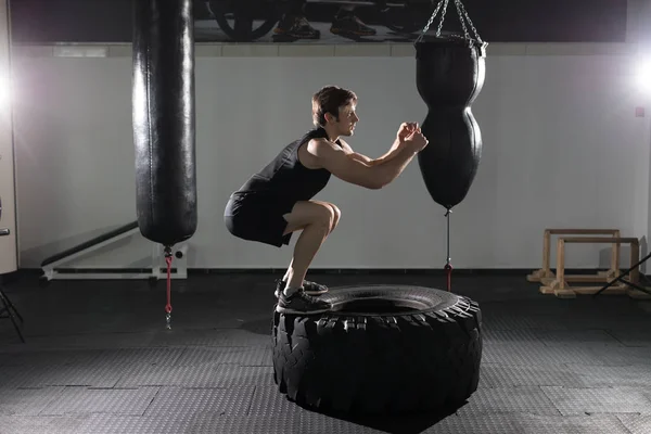 Entrenador personal volteando un neumático en un gimnasio mientras instruye a una modelo de fitness femenina cómo hacer el ejercicio . — Foto de Stock