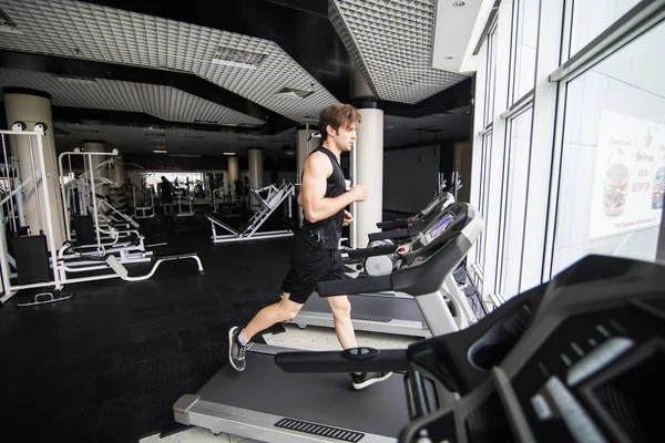 Spor salonunda koşu bandı üzerinde çalışan genç adam. yan görünüm