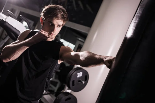Combatiente de kickbox muscular concentrado haciendo ejercicio con saco de boxeo en blanco en el gimnasio — Foto de Stock