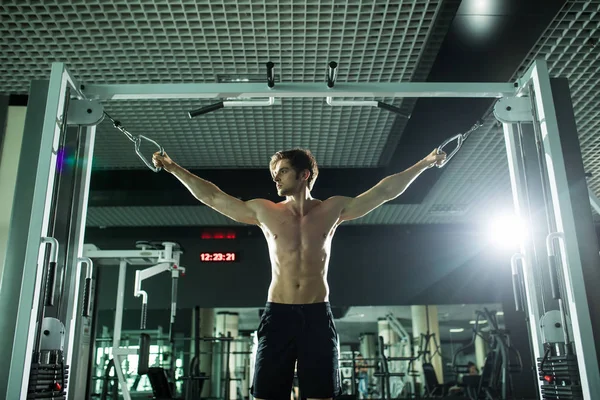 Bel homme fort faisant de l'exercice à la salle de gym avec machine . — Photo