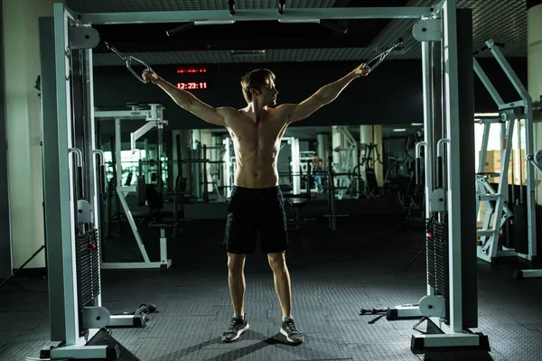 Starker schöner Mann, der im Fitnessstudio mit einem Gerät trainiert. — Stockfoto