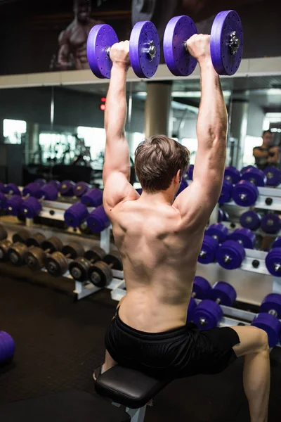 Вид сзади на молодого мужчину, делающего тяжелые упражнения с гантелями . — стоковое фото