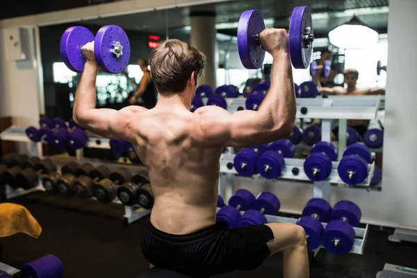 Achteraanzicht van een jonge man doen zwaar gewicht oefening met halters. — Stockfoto