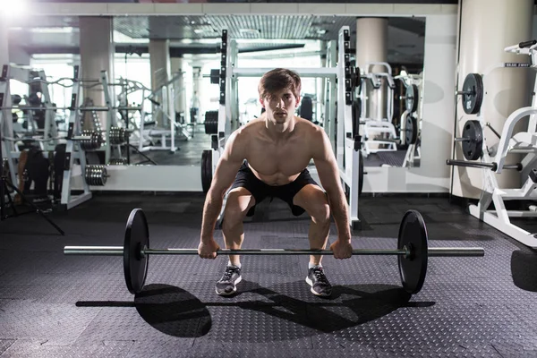 Homme musclé confiant s'entraînant squats avec des cloches au-dessus de la tête. Gros plan portrait de l'homme professionnel séance d'entraînement avec haltère à la salle de gym . — Photo