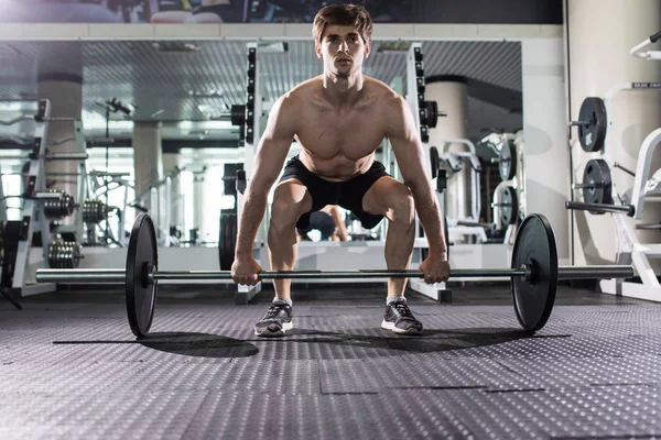 Jovem homem flexionando músculos com barra no ginásio. Desporto — Fotografia de Stock
