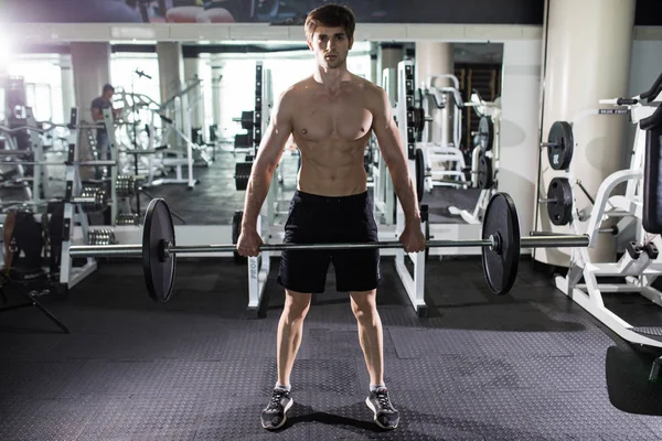 Νεαρός άνδρας λύγισμα των μυών με barbell στο γυμναστήριο. Αθλητισμός — Φωτογραφία Αρχείου