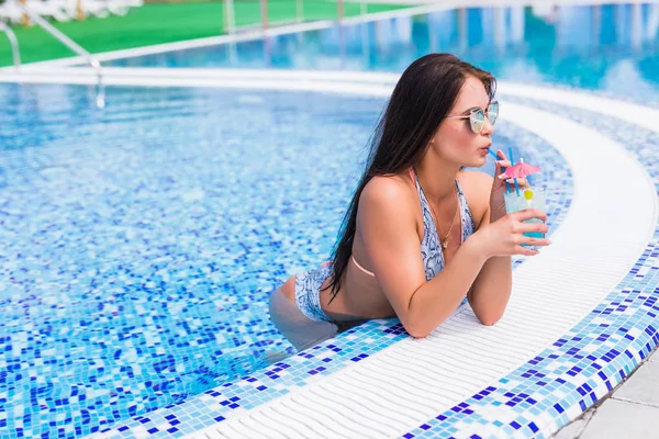 Соблазнительная девушка в синем платье отдыхает у бассейна у края бассейна. Молодая сексуальная женщина с тропическим коктейлем отдыхает. Досуг . — стоковое фото