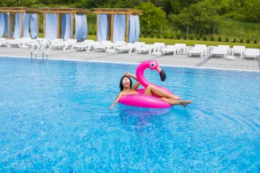 Tan kız şişme yatak flamingolar üzerinde oturur ve Havuzda rahatlayın. Havuz partisi