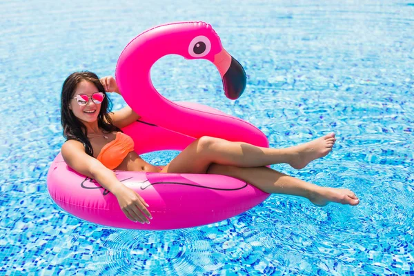 Mujer de belleza en un flamenco rosa en la piscina en gafas de sol — Foto de Stock