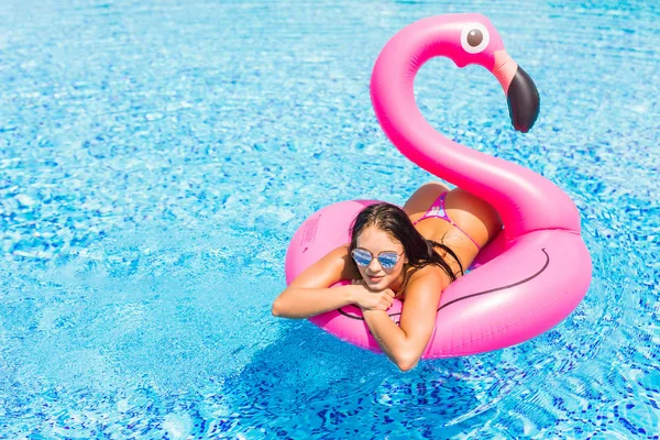 Красивая девушка сидит на надувных матрасе фламинго в бассейне и веселится. вечеринка у бассейна — стоковое фото