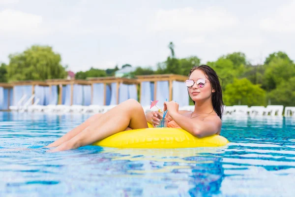 Sudaki şişme halkası üzerinde bir kokteylle güzel genç kadın