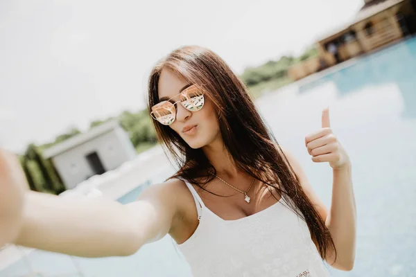 Retrato de menina bonita tirando uma selfie na piscina com os polegares para cima — Fotografia de Stock