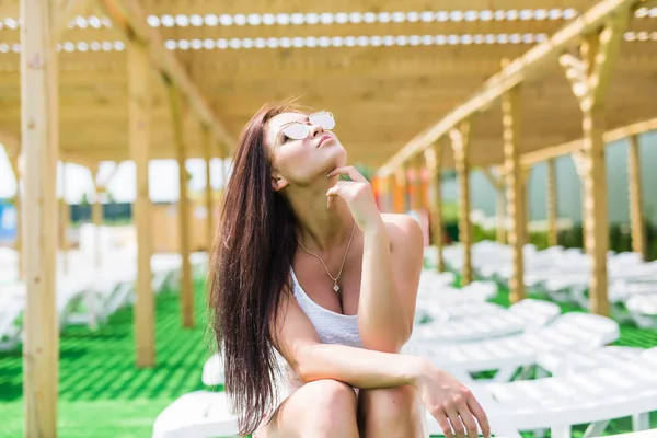 Mulher morena bonita com as mãos no queixo relaxante em uma espreguiçadeira ao ar livre perto da piscina — Fotografia de Stock