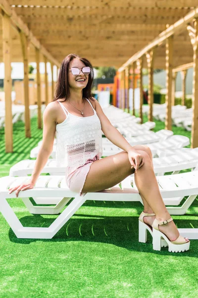 Jolie brune femme sourire relaxant sur une chaise longue en plein air près de la piscine — Photo