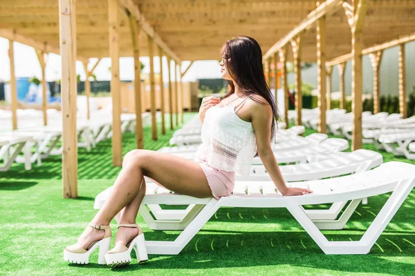 Bella donna bruna rilassante su un lettino all'aperto vicino alla piscina — Foto Stock