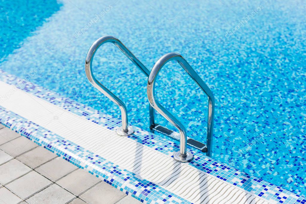 Grab bars ladder in the blue swimming pool. Summer.