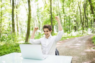 Mutlu çıktıktan iş adamı kaldırdı elleriyle yeşil park iş veya Ofis Masası, laptop önünde harika bir haber başarısını kutlamak. İş kavramı.