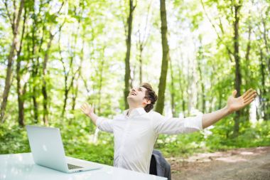 Mutlu çıktıktan iş adamı kaldırdı elleriyle yeşil park Ofis Masası, laptop önünde işindeki başarısını kutlamak. İş kavramı.